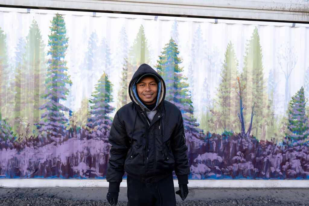 Troi, an artist who painted the mural, in front of his painted container